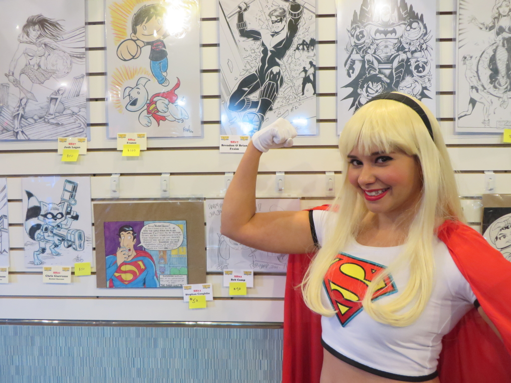 Diana as Supergirl posing by the comic art for the auction
