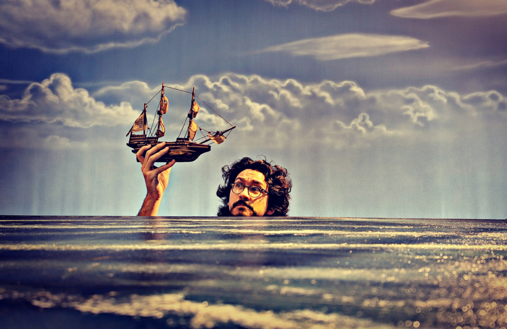 Ben Wickey holding a model ship behind an illustion of the ocean
