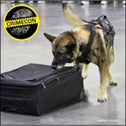 Aurora Police K9 German Shepherd dog, Jax, inspecting a suitcase; Crime Con logo in the top left.