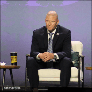 Agent Ash Thorne leaning forward in his seat on the stage.