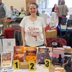 Amber wearing a Sisters in Crime t-shirt standing behind her author table