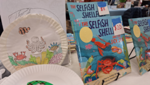 The Selfish Shellfish and the Sick Sea books on display next to a crayon-colored craft at an author table at Books in Bloom