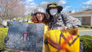 Left: Tracey Heisler holding her protest sign Right: Amber holding her banner Their arms around each others' back.