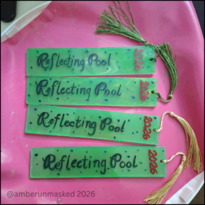 a silicone mat holding 4 resin art pieces: long neon green with speckled blue, hand-painted script, "Reflecting Pool" and "2026". Two have green tassels and the other two have gold tassels.
